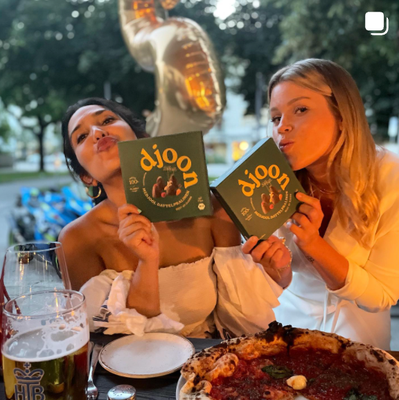 Zwei Frauen, die jeweils eine Packung Pralinen aus Datteln der Marke djoon halten und sie lecker finden.