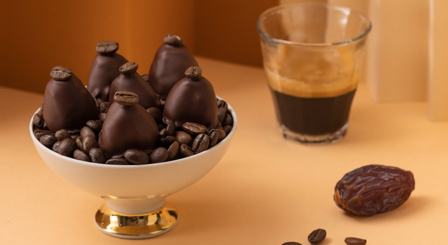 Tasse Kaffee oder Espresso mit Crema, einer Medjool Dattel, geröstete Kaffeebohnen und dazu Pralinen von djoon.