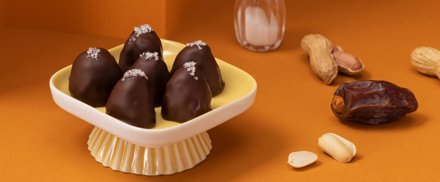 Schale mit mehreren djoon Dattelpralinen neben Erdnüssen, Salz und Medjool Datteln.