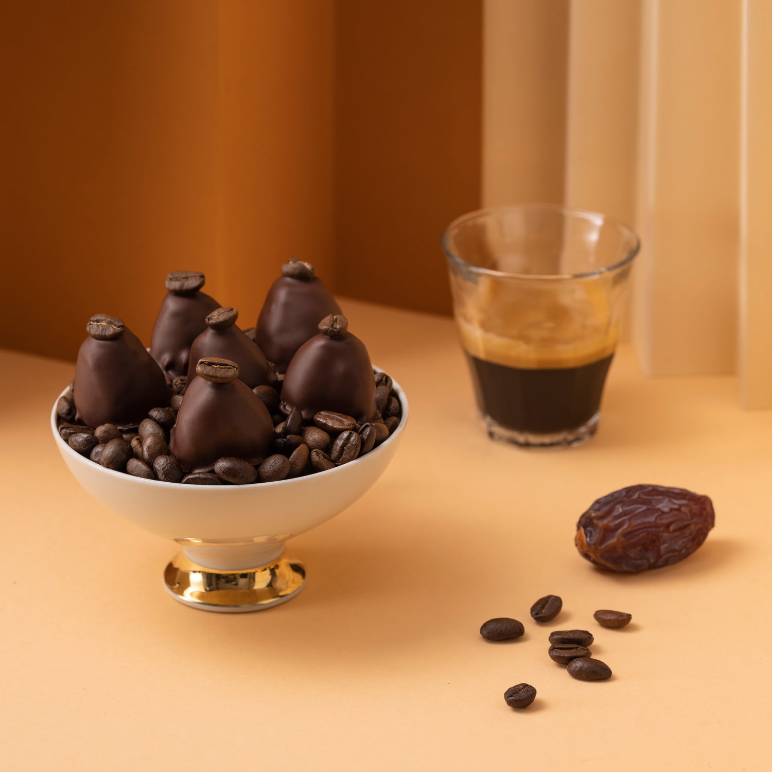 Tasse Kaffee oder Espresso mit Crema, einer Medjool Dattel, geröstete Kaffeebohnen und dazu Pralinen von djoon.