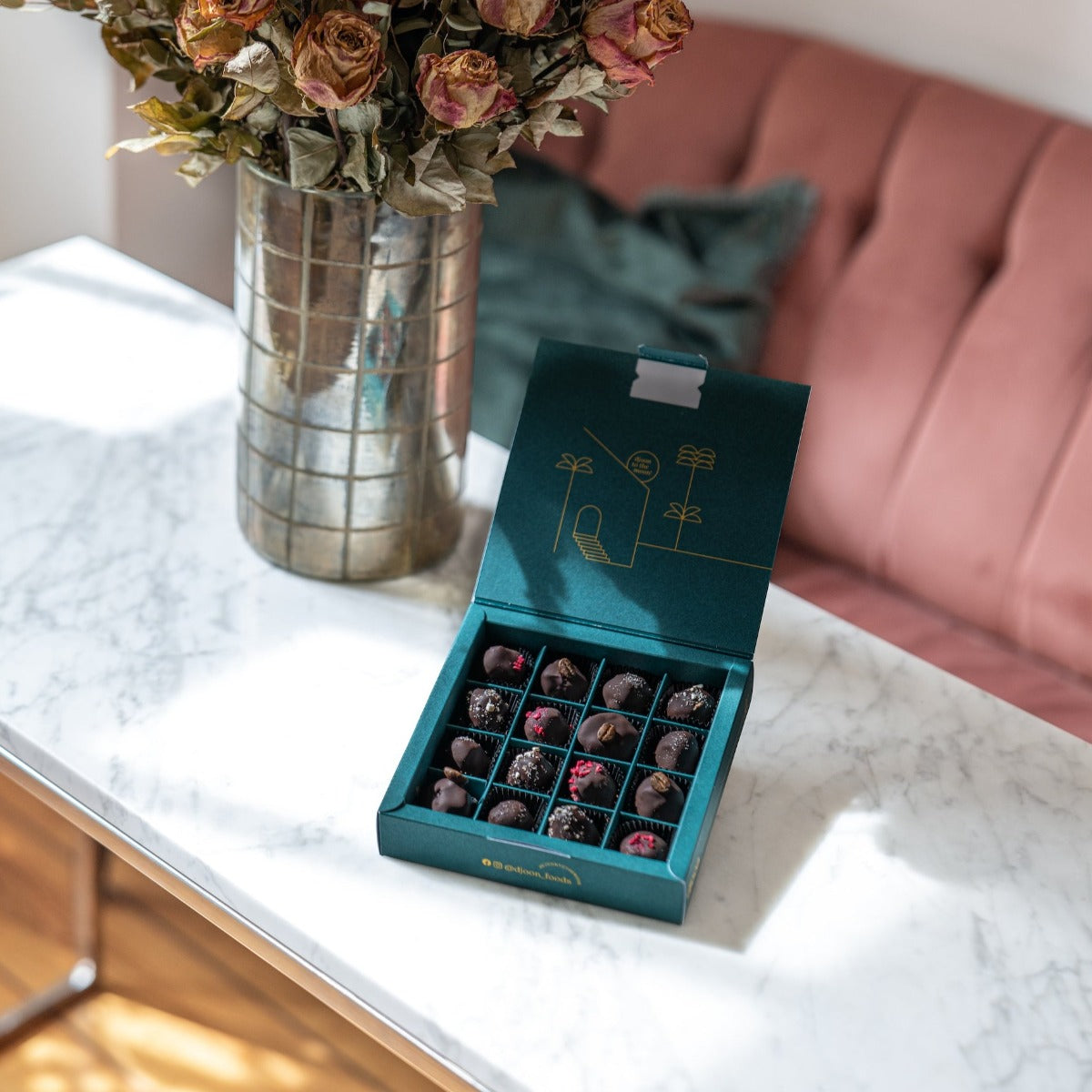 Offene Schachtel vegane Pralinen, überzogen mit 100Prozent Kakao auf einem Tisch mit einem Blumenstrauß